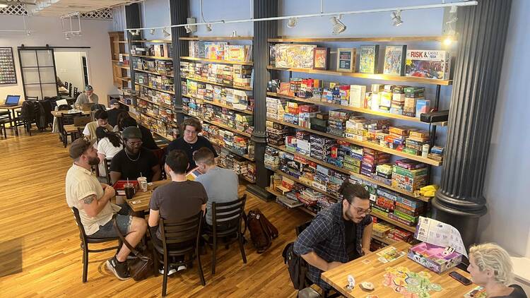 People sit at cafe tables playing games in front of colorful wall of games.