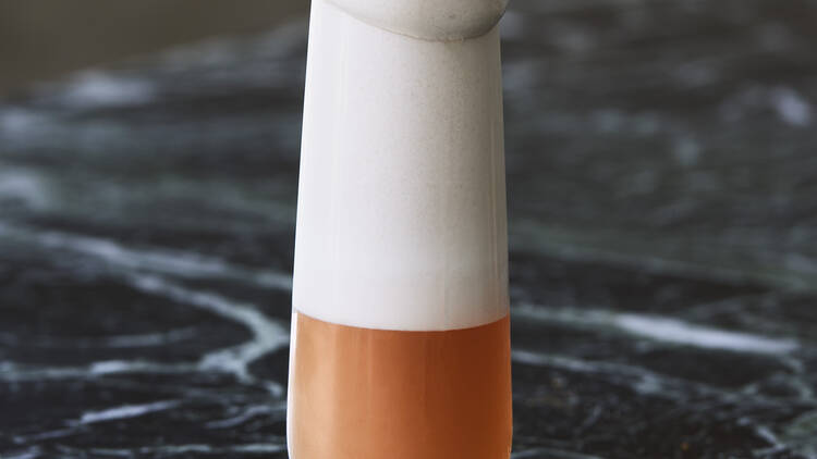 Foam-topped orange cocktail on a marble bar surface.