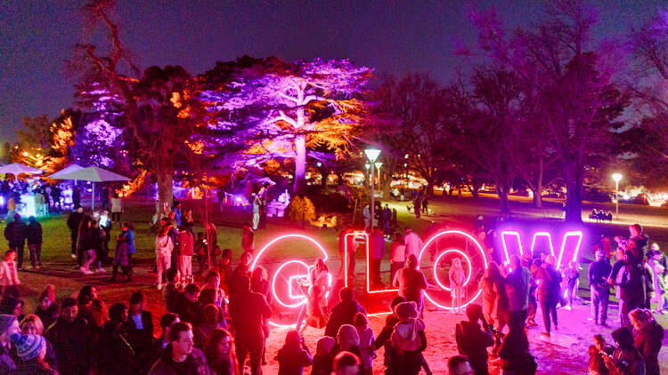 An outdoor night festival with a large neon sign that says 'GLOW'.