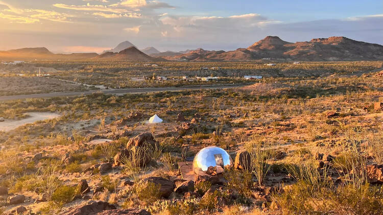 At sunset, warm light washes over a desert landscape with one shiny silver pod in the middle.