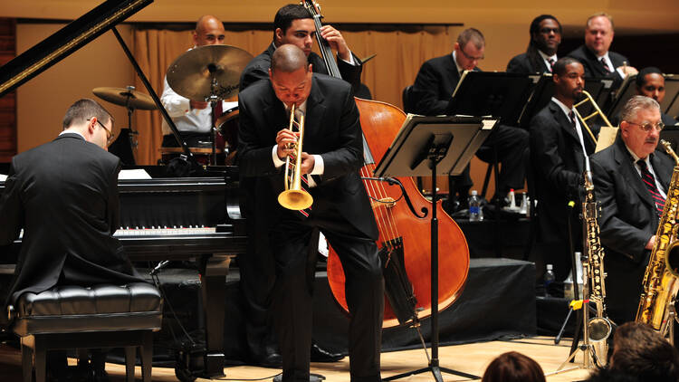 A black man plays the trumpet as part of an orchestra.