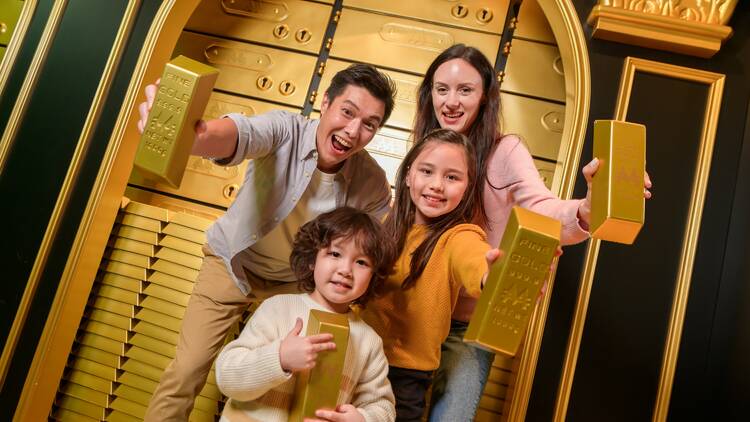 A family posing with gold bullions in front of more gold.