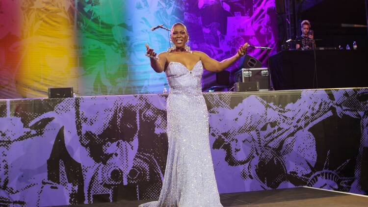 Performer wearing a sparkly silver dress on a stage with rainbow lighting.