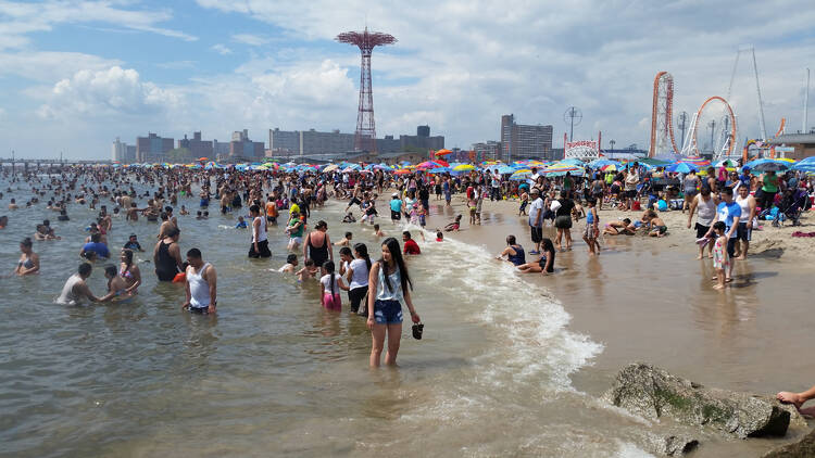 People swim at Coney Island beach with the amusement park in the background. 