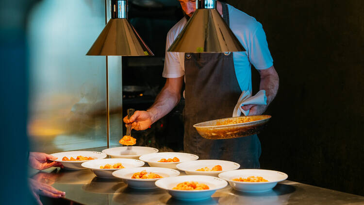 Chef spooning pasta into bowls.