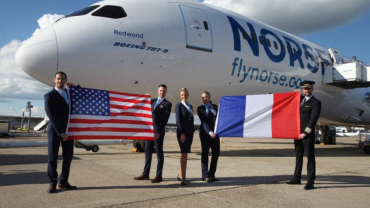Five crew members stand in uniform in front of a Norse Dreamliner holding an American flag and a British flag