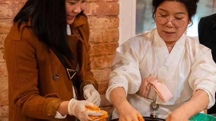 Korean grandmother teaching event guest how to make kimchi.