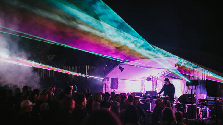 A person plays an outdoor nighttime gig with laser lights.