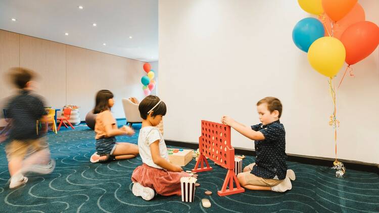 Kids play connect four next to some balloons