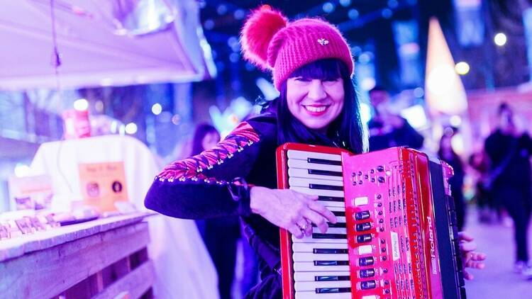 A woman wearing a red beanie plays a red accordion 