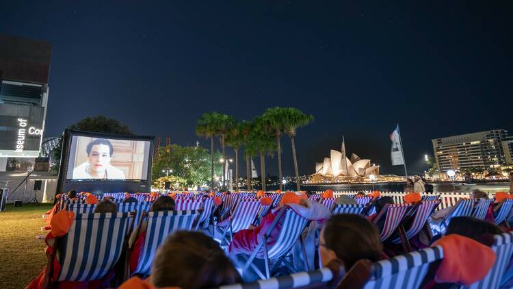 People in deck chairs watch a film with the Sydney Opera house in the background