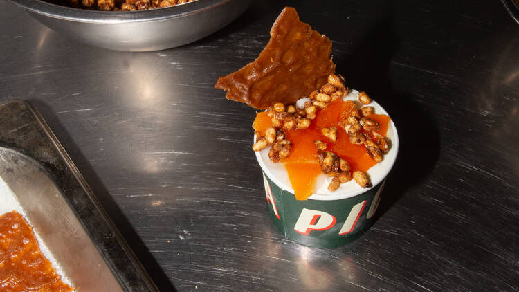 Cup of ice cream with nut brittle and cracker topping.