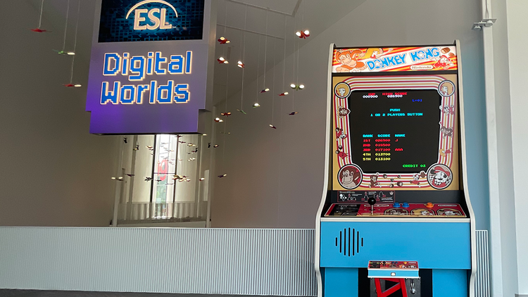 The Donkey Kong game is perched next to an atrium overlook with a sign reading "ESL Digital Worlds" hanging from the ceiling