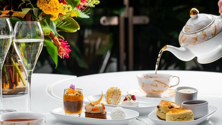 A teapot pours into a cup behind a selection of treats