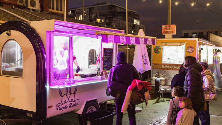 A neon-lit food truck at an outdoor market.