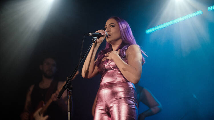 A singer with purple hair in a shiny pink jumpsuit.