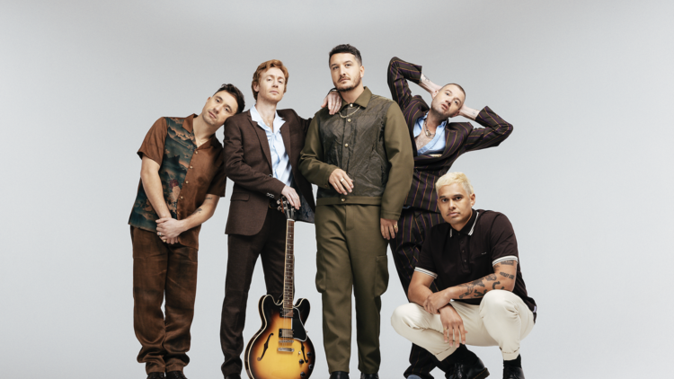 New Zealand's biggest band, Six60, standing together wearing brown clothes, with a guitar.