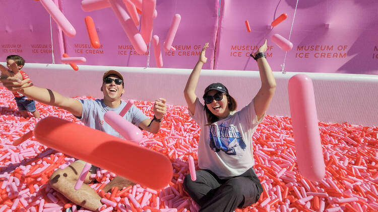Two people toss pink and red sprinkles into the air at the sprinkle pool.