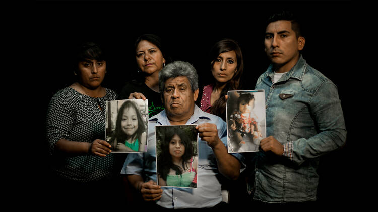 A family holding photos of young women as part of the Part of the Missing Peoples + Femicides Annex Group Show.