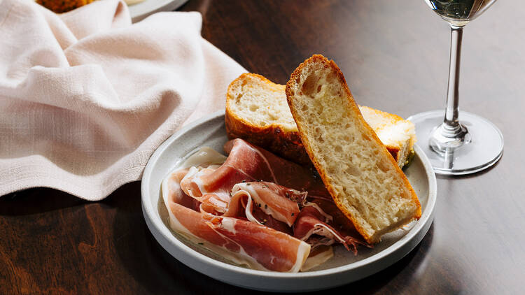 A plate with bread and prosciutto on a table.