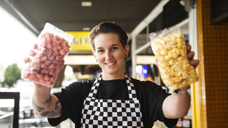 Woman in a checkered apron holding up two bags of assorted popcorn.
