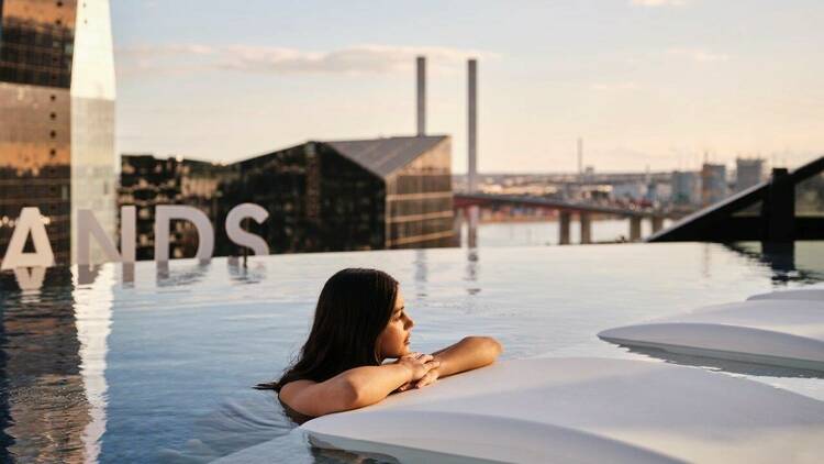 A woman in an infinity pool with a view of the Bolte Bridge