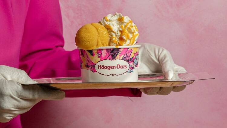 Person in a pink blazer and white gloves holding a pot of Haagen-Dazs ice cream