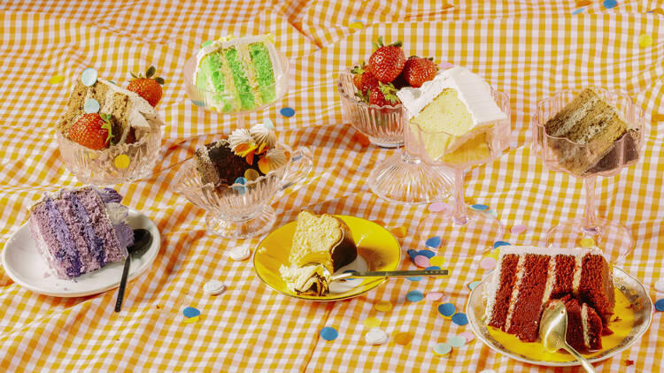 Assorted colourful layer sponge cakes plated up on an orange and white gingham rug.