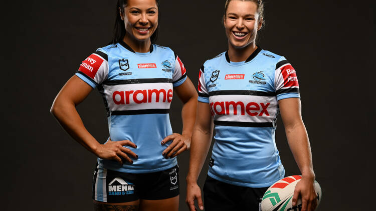 Two women in blue football jerseys, holding a football. 