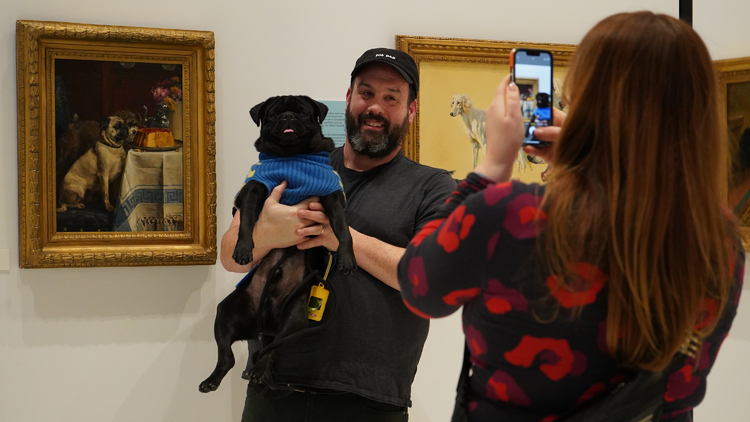 A man poses with his dog next to a piece of artwork.