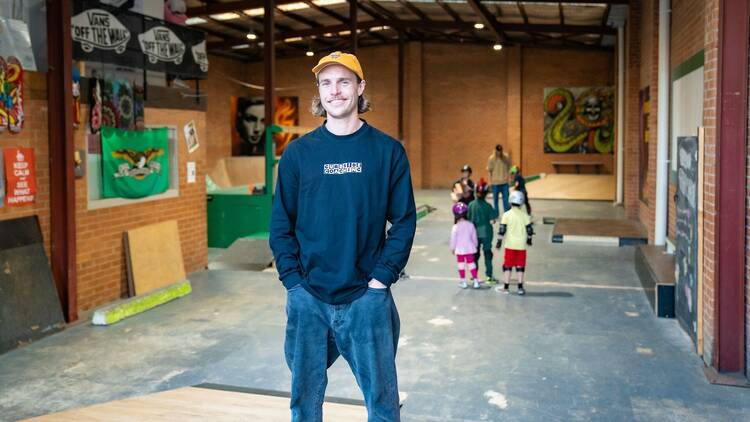 A man wearing a cap stands in front of a kids skate lesson.