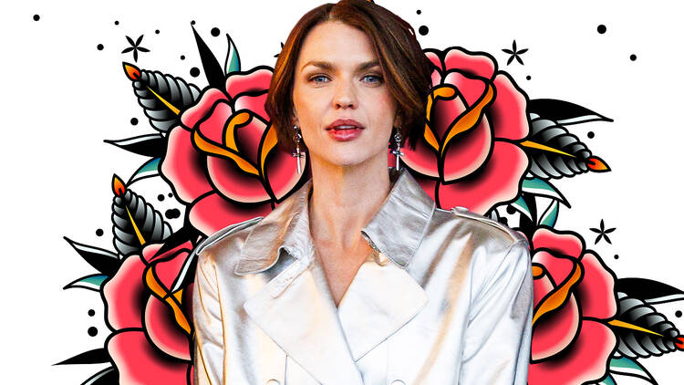 Ruby Rose in a silver trenchcoat against a backdrop of roses.