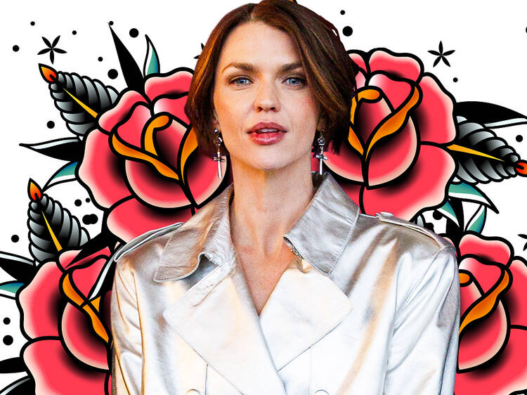 Ruby Rose in a silver trenchcoat against a backdrop of roses.