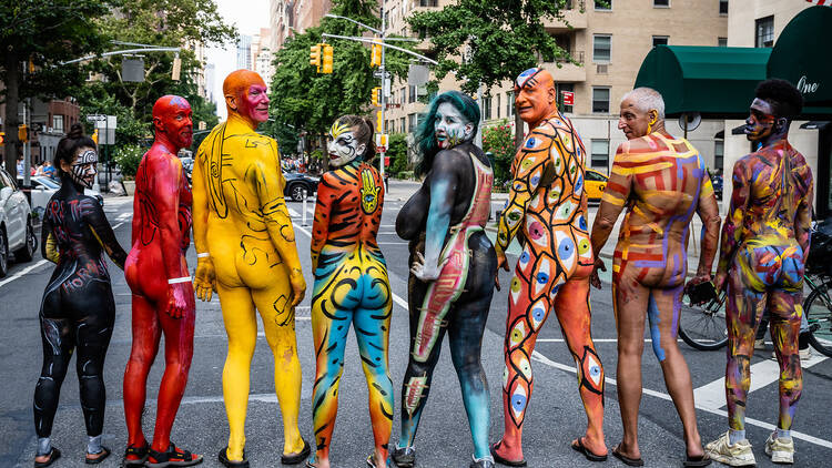 Seven models stand with their backs toward the camera; each one is painted from head to toe.