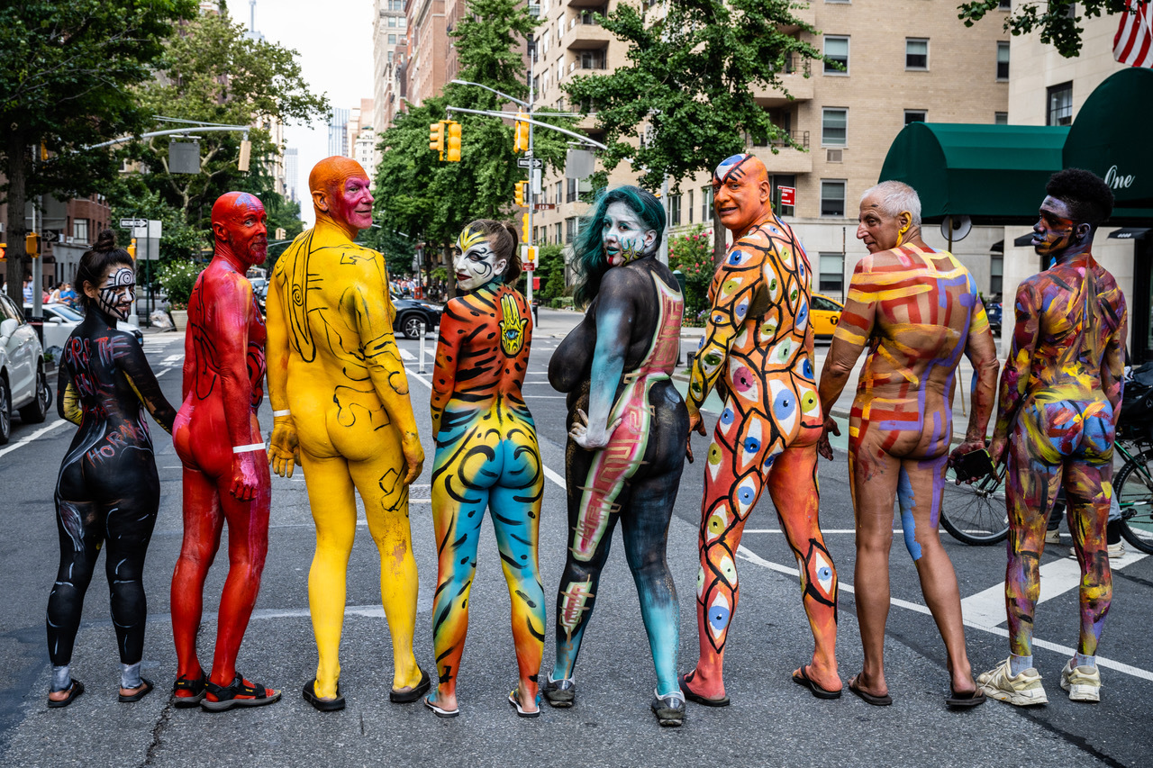 Seven models stand with their backs toward the camera; each one is painted from head to toe.