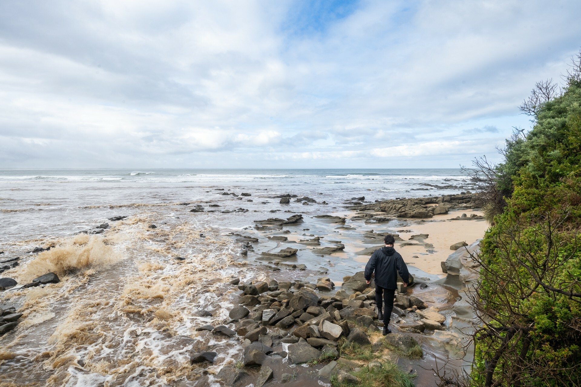 A man walks on a rocky shoreline.