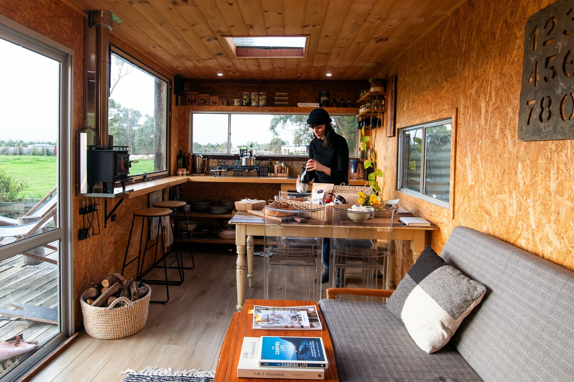 A woman opens a bottle of wine at the kitchen table in a cabin at Wattle Bank Farm