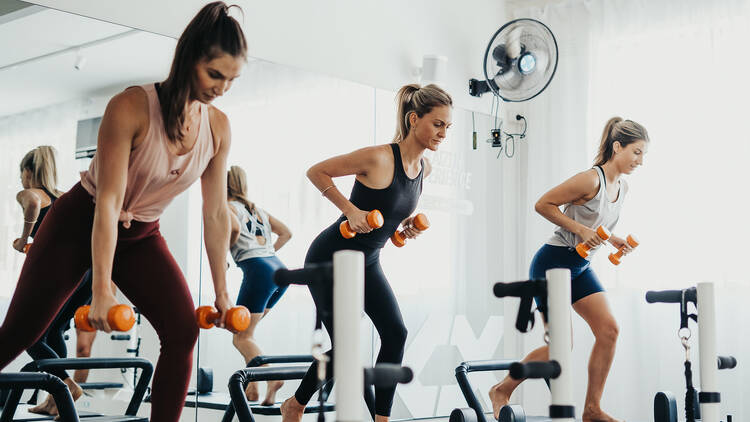 Three women holding dumbbells on pilates reformers.