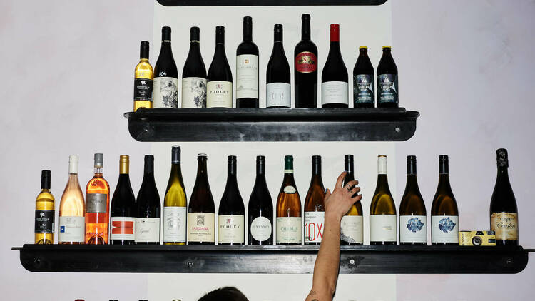 Bartender reaching for bottles of wine from a set of black shelves.