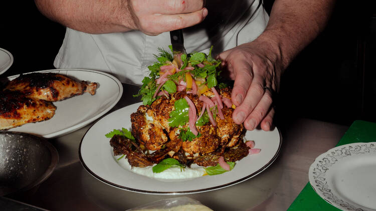 Chef cutting into a herb-decorated whole-roasted cauliflower.