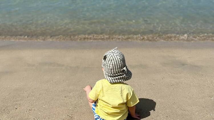 A toddler sits on the beach, enjoying a stress-free family trip