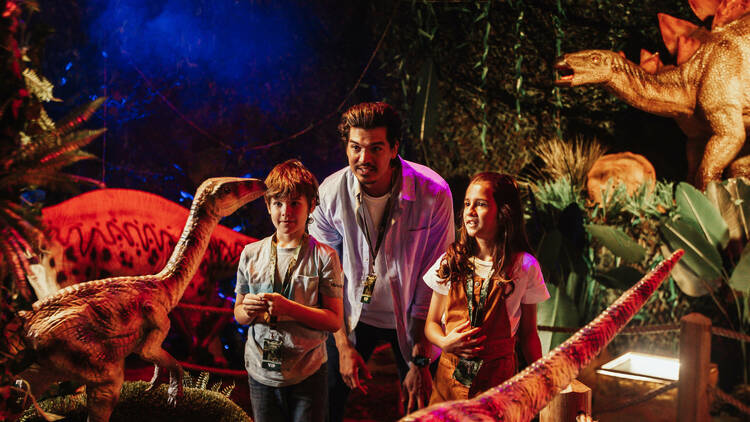 A man and two kids looking at some dinosaurs.