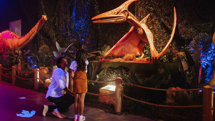 A man and two children looking at a dinosaur.