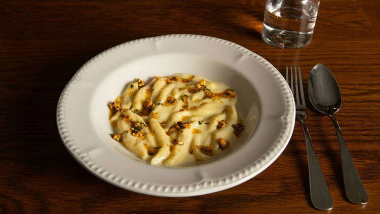 Plate of gnocchi with cutlery and a glass of water on a wooden table.