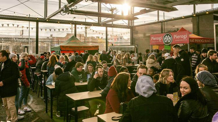 A busy food truck park in late afternoon sunlight.