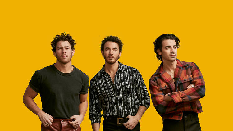 The Jonas Brothers standing against a yellow backdrop.