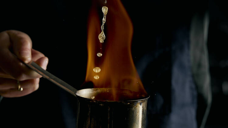 Bartender pouring liquid into a flaming pan.