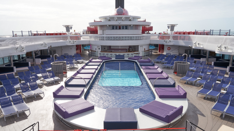 A cruise ship deck with a pool, sun beds and deck chairs around