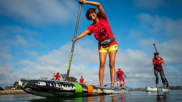 A woman on a stand-up paddleboard wearing a red WWF shirt.