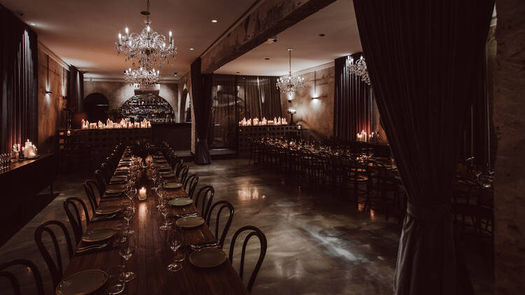 A dimly lit function room lined with tables and candles. 